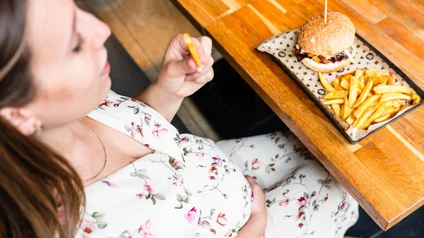 Burger eating pregnant woman. Pretty young pregnancy girl eat tasty hamburger. Junk food concept