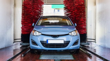 Araba yıkama makinesi. Otomatik yıkama istasyonunda otomatik fırçayla temizlenmiş mavi araba. Otomatik oto yıkama makinesi arkaplanı