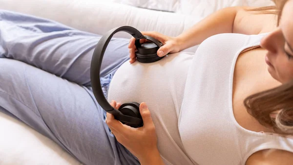 Pregnancy music woman listen. Pregnant woman listening to music. Mother belly listen headphones sound. Concept of pregnancy, maternity, expectation for baby birth.