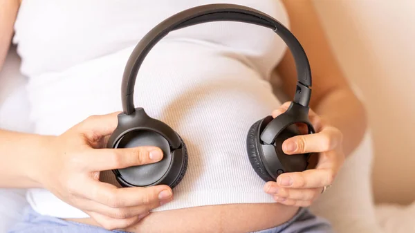Baby music pregnancy woman. Cheerful pregnant girl relaxing listening music in headphones. Mother belly listen headphones sound. Therapy, healthcare, motherhood concept