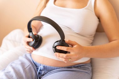 Bebek müziği hamile kadın. Neşeli hamile kız kulaklıkla müzik dinliyor. Anne göbek kulaklık sesi duyuyor. Terapi, sağlık, annelik kavramı.