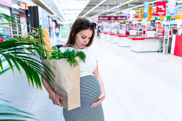 Woman shopping food grocery. Pregnant woman with healthy green vegetables, fresh tomato in market food bag on grocery supermarket background. Healthy food background