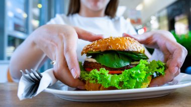 Vejetaryen sandviçi sağlıklı vejetaryen burger. Salata, avokado ve sebzeli vejetaryen burger yiyen sevimli bir kız. Vejetaryen diyet gıda konsepti