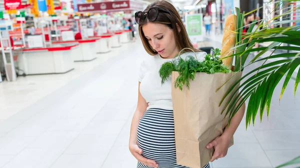Woman supermarket grocery food bag. Pregnancy mother with healthy vegetables, fresh lettuce salad leaves in market food bag on grocery supermarket background. Everyday shopping concept
