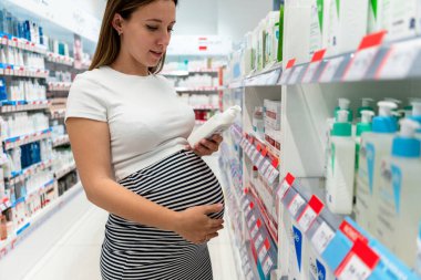Eczane tezgâhında hamile bir kadın. Perakende satış yapan eczanenin mutlu hamile müşterisi. Hamilelik, ilaç sağlık konsepti