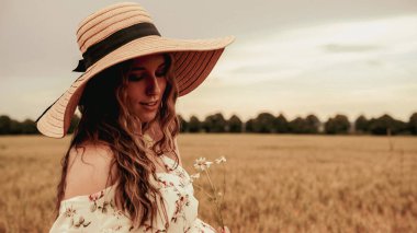 Güzel, romantik bir kız. Güneş şapkalı mutlu genç kadın gün batımında buğday tarlasında. Kopyalama alanı, günbatımı, ışık, yaz mevsimi. Boho şık tarzı
