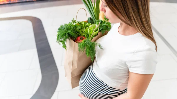 Woman supermarket grocery food bag. Pregnancy mother with healthy vegetables, fresh lettuce salad leaves in market food bag on grocery supermarket background. Everyday shopping concept