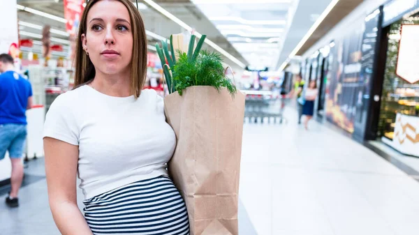 Woman food shopping pregnancy. Pregnant mother with healthy lettuce salad leaves, fresh tomato in market food bag on grocery supermarket background. Healthy food background