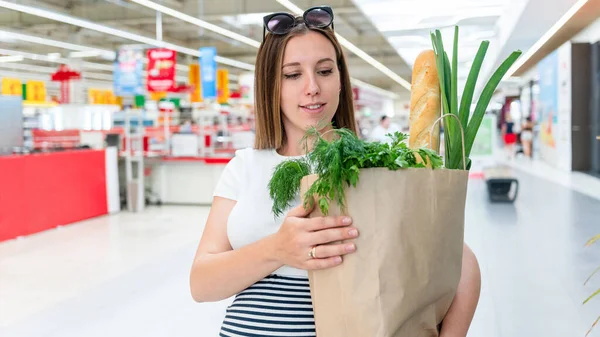 Woman food shopping pregnancy. Pregnant mother with healthy lettuce salad leaves, fresh tomato in market food bag on grocery supermarket background. Healthy food background