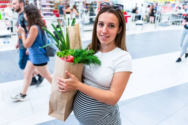 Pregnant food bag supermarket. Pregnancy woman with healthy lettuce salad leaves, fresh tomato in market food bag on grocery supermarket background. Everyday shopping concept