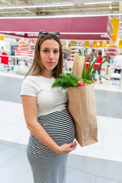 Pregnant supermarket food bag. Pregnancy woman with healthy fruit, fresh tomato in market food bag on grocery supermarket background. Shopping food supermarket concept
