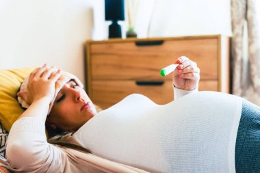 Hamilelik ateşi kontrolü. Hamile kadın termometre tutuyor, ateşi kontrol et. Hamile kız hasta. Gebelik, hamilelik, doğum