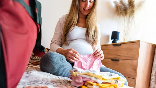 妊娠中のベビー服 黄色の赤ちゃんの服を着た美しい妊婦さん 妊娠中の女性は腹を抱え 妊婦病院の袋を詰める コンセプト妊産婦妊娠出産 — ストック写真