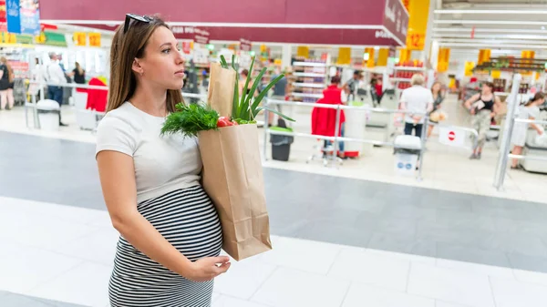 Pregnant food bag supermarket. Pregnancy woman with healthy lettuce salad leaves, fresh tomato in market food bag on grocery supermarket background. Everyday shopping concept
