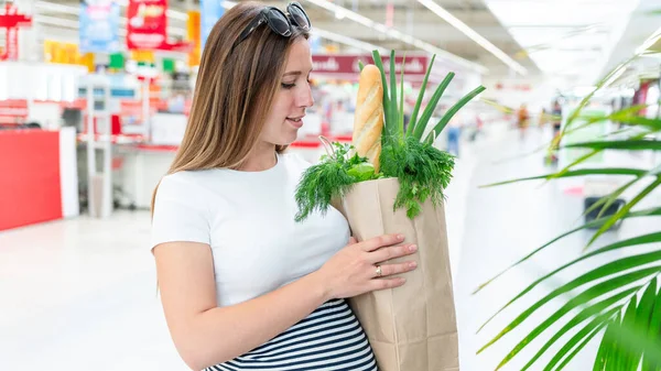 Pregnant healthy food bag. Pregnancy woman with healthy vegetables fresh, lettuce salad leaves in market food bag on grocery supermarket background. Healthy food background