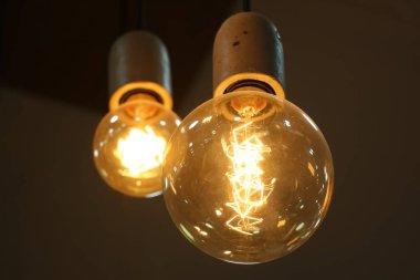 İki klasik akkor Edison tipi ampul koyu bir arkaplanda parlıyor. Çatı katı stili dekorasyonu
