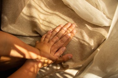Ebeveynlerin ve çocukların elleri, arka planda kahverengi bir kumaş ve güneş ışığı. Aile ve destek kavramı. Üst görünüm