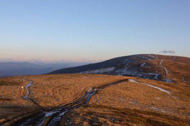 Karpat Dağları 'nda sonbahar manzarası. Borzhava sırtında karlı toprak yol. Gün batımı aydınlatma