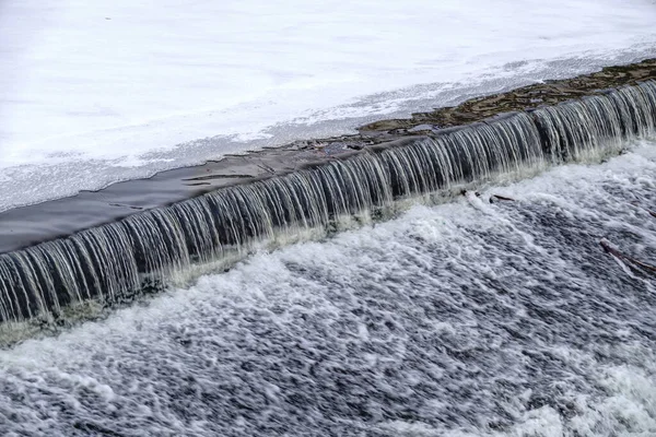 A small flat cascade in a calm river with ice in winter. Water background