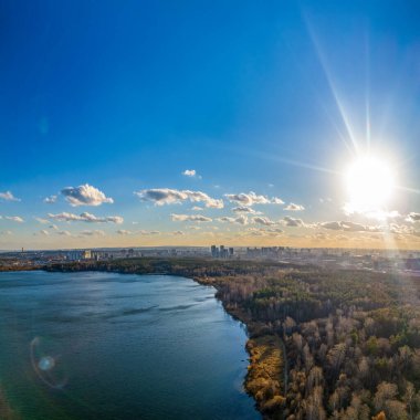 Gün batımında göl kıyısında sonbahar ormanı ve ufukta şehir, mercan manzarası. Shartash Gölü ve Yekaterinburg, Rusya