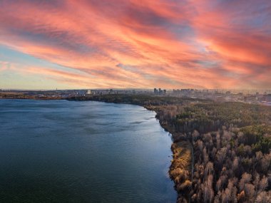 Gün batımında göl kıyısında sonbahar ormanı ve ufukta şehir, mercan manzarası. Shartash Gölü ve Yekaterinburg, Rusya