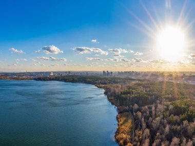 Gün batımında göl kıyısında sonbahar ormanı ve ufukta şehir, mercan manzarası. Shartash Gölü ve Yekaterinburg, Rusya