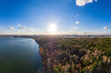 Gün batımında göl kıyısında sonbahar ormanı ve ufukta şehir, mercan manzarası. Shartash Gölü ve Yekaterinburg, Rusya