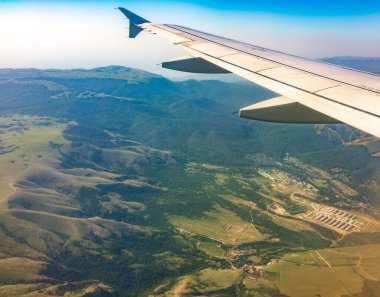İniş sırasında uçak kanadı, mavi gökyüzü ve yeşil kara manzarası. Uçak penceresi manzaralı. Dünya ve gökyüzü bir uçağın penceresinden görüldüğü gibi.