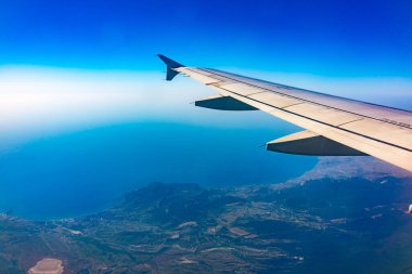 Güzel, açık mavi bir gökyüzü ve uçak kanadının penceresinden manzarayı izleyin. Dünya ve gökyüzü bir uçağın penceresinden görüldüğü gibi.