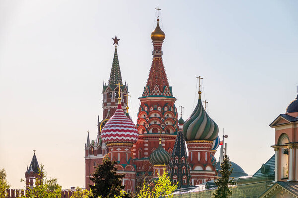 Multi-colored domes of St. Basil's Cathedral and the Spasskaya Tower of the Moscow Kremlin around the trees. Symbols of the Russian state. Summer trip to Moscow. Tour to Russia. Religious tourism