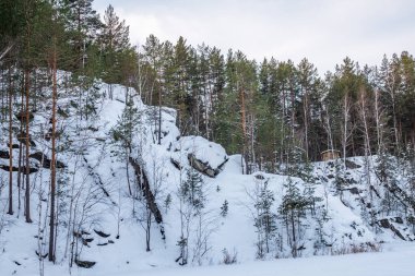Rusya 'da kış mevsiminde Yekaterinburg yakınlarındaki Sysert kasabasında bulunan Talc taş ocağının etrafındaki sarp kayalıklar. Karla kaplı bir kayanın üzerinde çam ve huş ağacı