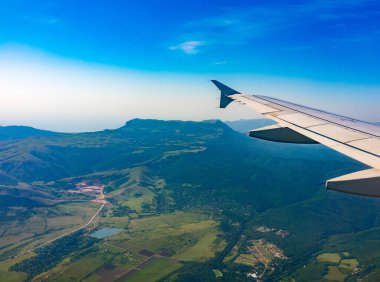 İniş sırasında uçak kanadı, mavi gökyüzü ve yeşil kara manzarası. Uçak penceresi manzaralı. Dünya ve gökyüzü bir uçağın penceresinden görüldüğü gibi.