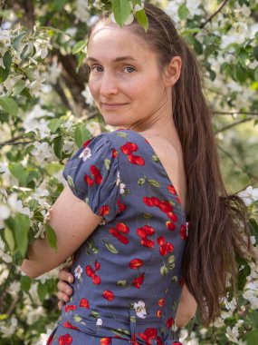 Bahar parkında çiçek açan ağaçların arasında makyajsız güzel bir genç kadın. Doğal makyajsız, başını yeşil arka plana eğmiş bir kızın yakın plan portresi. Bahar geliyor..