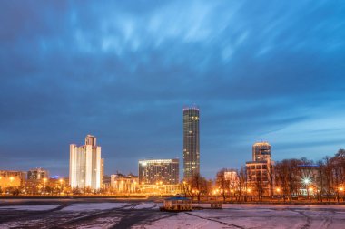 Şehir merkezindeki göletin kıyısında bahar gecesi erken saatlerde. Aydınlatılmış binalar. Bahar geldi. Nehirdeki buz erimeye başladı. Yekaterinburg, Rusya