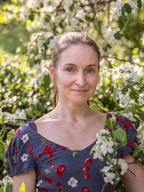 Bahar parkında çiçek açan ağaçların arasında makyajsız güzel bir genç kadın. Doğal makyajsız, başını yeşil arka plana eğmiş bir kızın yakın plan portresi. Bahar geliyor..