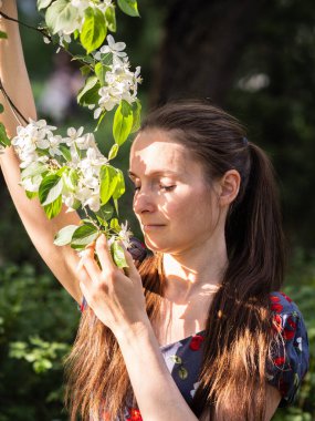 Bahar parkında çiçek açan ağaçların arasında makyajsız güzel bir genç kadın. Doğal makyajsız, başını yeşil arka plana eğmiş bir kızın yakın plan portresi. Bahar geliyor..