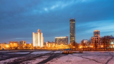 Şehir merkezindeki göletin kıyısında bahar gecesi erken saatlerde. Aydınlatılmış binalar. Bahar geldi. Nehirdeki buz erimeye başladı. Yekaterinburg, Rusya