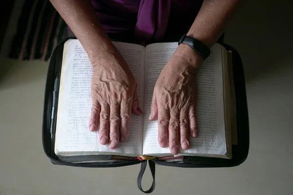 老妇人皱着眉头摸着一本打开的中国圣经 顶部视图 — 图库照片