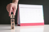 Ruka na 2022 dřevěné kostky s kalendářem v pozadí. Nový rok, nový začátek. Kopírovat prostor.