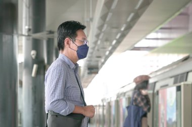 Metroda durup trene binmeyi bekleyen yüz maskeli Asyalı bir adam. Maskeli geçiş kavramı.