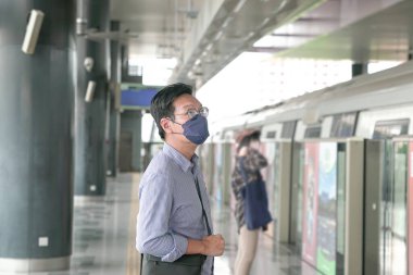 Metroda durup trene binmeyi bekleyen yüz maskeli Asyalı bir adam. Maskeli geçiş kavramı.