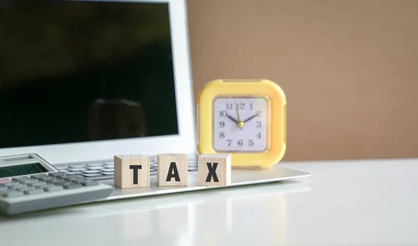 ラップトップの上と電卓とクロックの横にある木製のキューブ上の単語税 税務申告の概念 — ストック写真