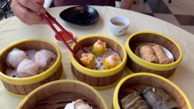 Bir parça et almak için çubuk kullanan bir adam, bambu sepetinden mai kuşatma, restoranda bir Dim Sum tabağı.