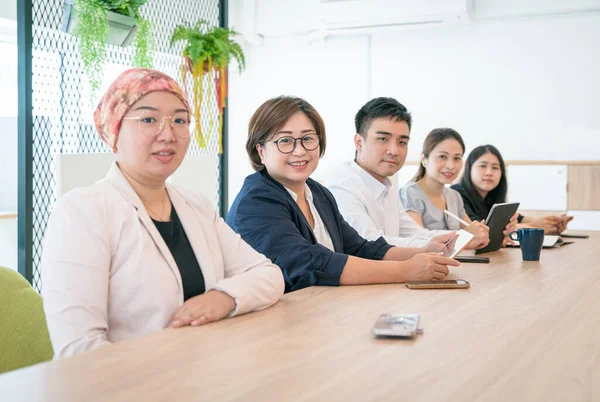 Portrait of a group of Asian corporate colleagues sitting together in a row, in a modern office.