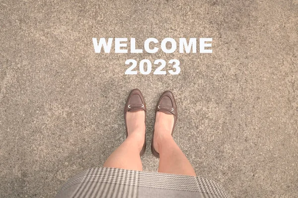 Top view of businesswoman feet with heels standing on asphalt road and text Welcome 2023. Happy new year 2023 concept.