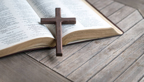 Wooden cross on top of an open bible and wood table. Copy space.