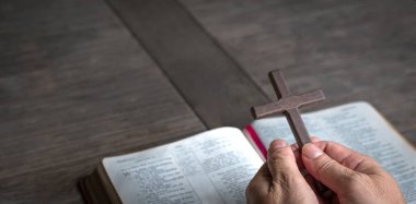 Kutsal İncil 'in üstünde haç tutan bir el. Hristiyan inancı ve bağlılık kavramı. Boşluğu kopyala.