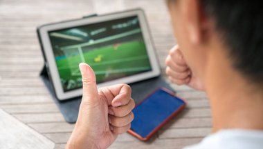 Man with thumbs up while watching football sports game on digital tablet. Live stream or sports online concept. clipart