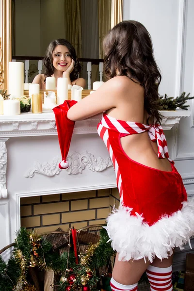 Portrett av en vakker ung kvinne i nisseklær som ser i speilet på julens bakgrunn . – stockfoto