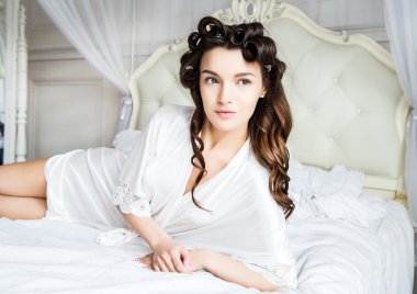 Beyaz ipek iç çamaşırlı güzel gelin bir sabah yatağında uzanıyor.